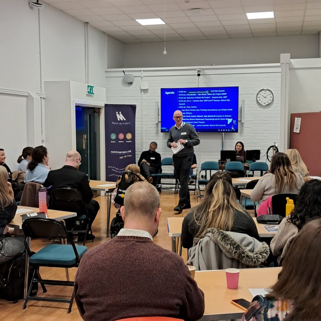 Photo of attendees gathered for the Oxford City Council matching event, facing a presenter and screen at the front of the room.