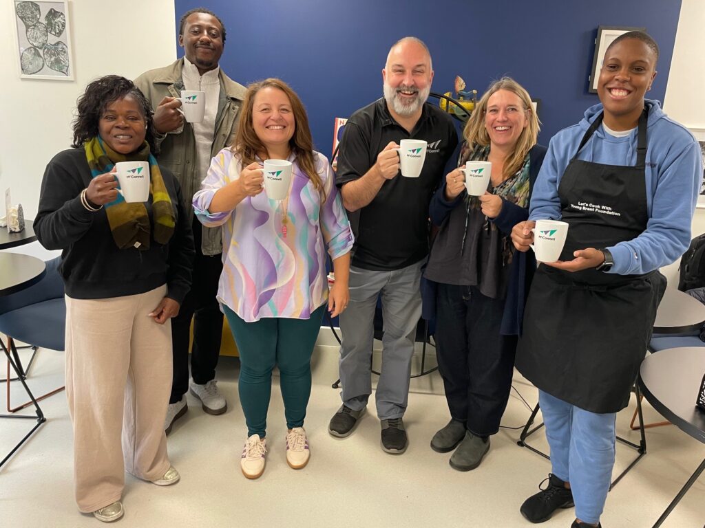 Julian Sanz, Head of Social Value at McConnell, and five team members from the Young Brent Foundation smile while holding donated coffee mugs for their new  project - a coffee shop.