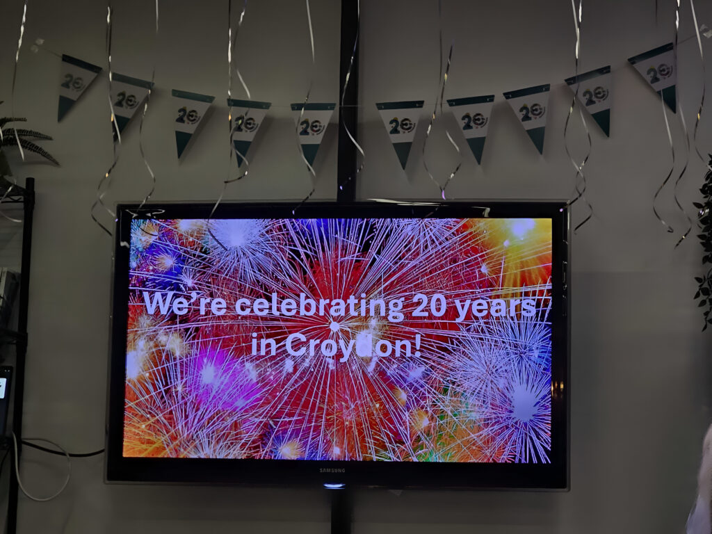 Screen displaying the text 'We're celebrating 20 years in Croydon',  with party bunting above, at the Croydon Procurement and Social Value event celebrating 20 years of Croydon's Social Value Programme, Croydon Commitment.