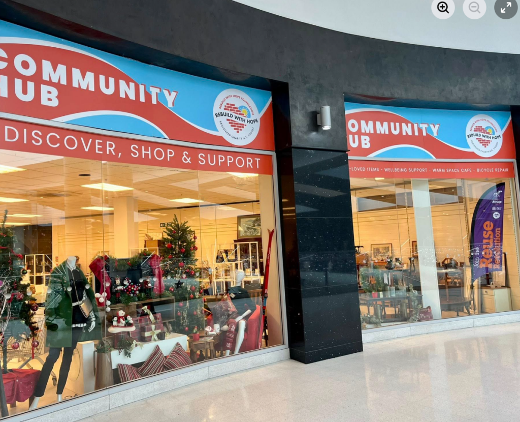 The exterior of Rebuild with Hope's community hub in the Grand Arcade shopping centre, featuring new signage reading "Community Hub — Discover, Shop & Support" alongside the Rebuild with Hope Foundation logo, showing the potential of what business partnerships can do.