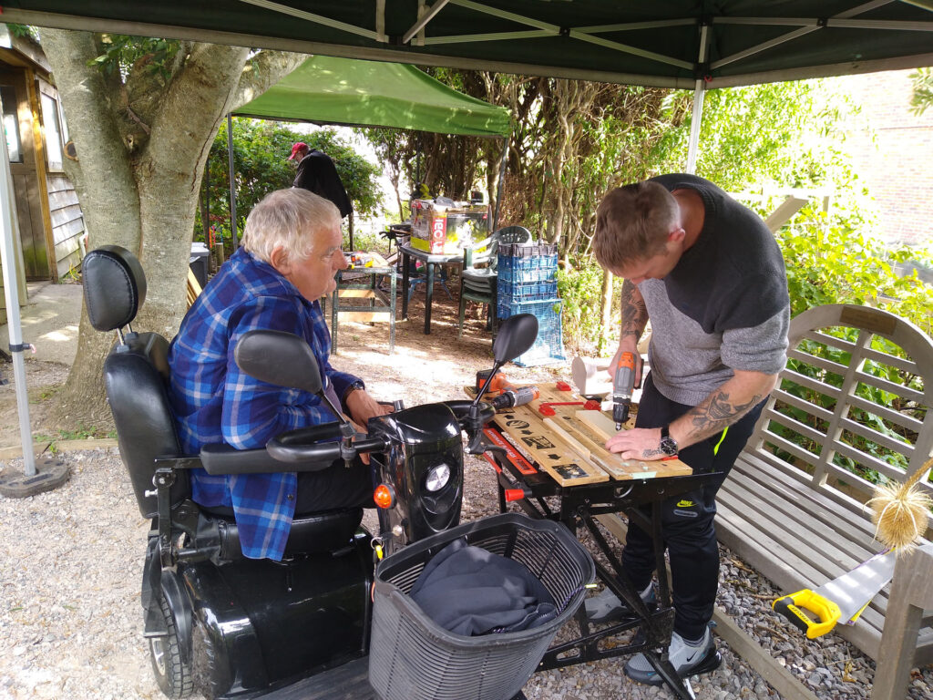A volunteer from Petworth Community Garden CIC assists a session participant who uses a wheelchair as they do woodwork together.