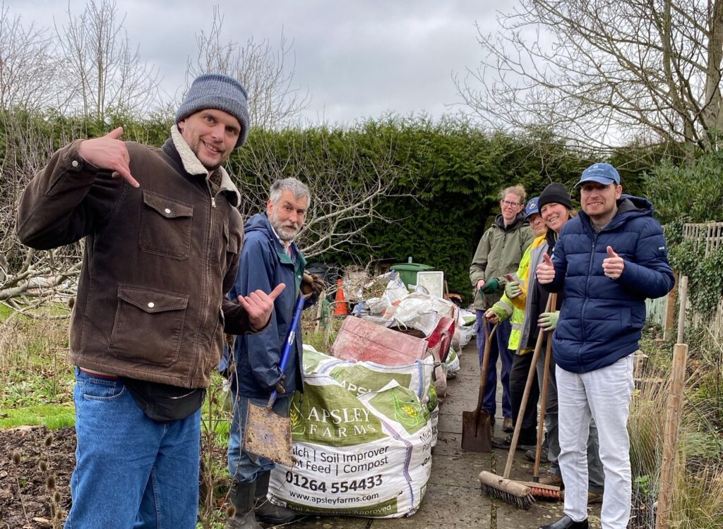 6 smiling volunteers and local residents with additional needs stand in the Wantage Market Garden alongside 730l of soil improver donated by Advanced Maintenance UK via Match My Project.