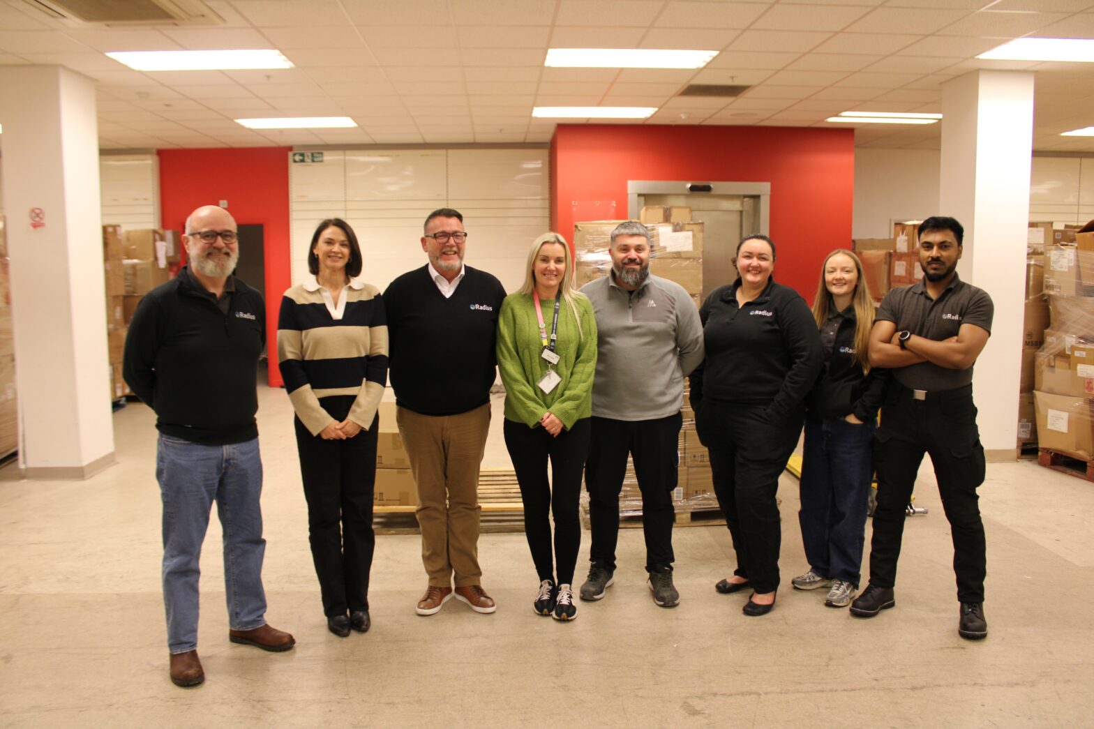 Radius volunteers and Rebuild with Hope team members standing together in the warehouse, surrounded by rails of donated clothing.