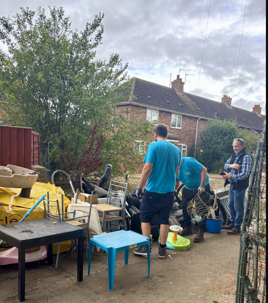 Three volunteers clearing a large pile of unwanted furniture and household items in a residential area in Oxford during a community cleanup day.